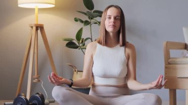 Evde yoga meditasyonu. Denge ve sağlık için egzersiz. Sağlıklı genç bir kadın halının üzerinde oturup lotus pozu alıyor, evde meditasyon yapıyor, gözlerini kapatıyor konsantre olmaya çalışıyor..
