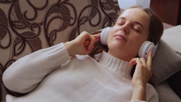 Ευτυχισμένη Γυναίκα Ξαπλωμένη Στον Καναπέ Ακούγοντας Μουσική Μέσω Ασύρματων Ακουστικών — Αρχείο Βίντεο