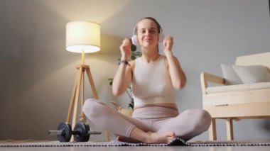 Kulaklıkla egzersiz. Neşeli, neşeli sportif kadın bej spor giysisi ve kulaklık takmış müzik dinliyor spor sonrası antrenmandan sonra dans ediyor..