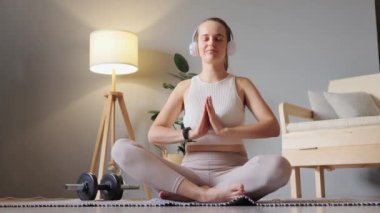 Rahatlama ve sağlık için müzik. Kulaklık takan, özel bir meditasyon yapan evde yoga yapan bir kadın zor bir haftadan sonra avuçlarını dua ederek rahatlatıyor..