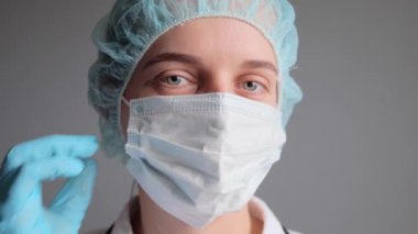 Üniformalı tıbbi eldiven ve maske takan çekici kadın doktor ya da hemşire hastanede tıbbi yardım yaparken kameraya bakıyor..