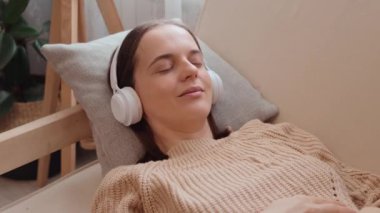 Sakin sakin kadın, örülü süveter giyip evde kulaklıkla müzik dinliyor. Gözlerini kapatıyor ve cep telefonunda meditasyonun tadını çıkarıyor..
