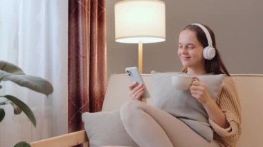Kulaklıkla müzik dinleyen, kahve içen, çay içen, cep telefonunu internete takıp hafta sonunun keyfini çıkaran çekici bir kadın..