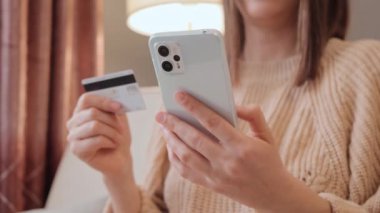 Elinde akıllı telefon ve bankacılık kartı bulunan tanınmayan bir kadın, evde internet üzerinden yapılan mobil alışverişe dahil olmuş, kadın alışverişçi internet mağazasından mal veya hizmet satın alıyor..