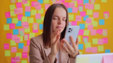 Ofiste bilgisayarla duvara karşı poz verirken akıllı telefon kullanan iş kadını şok oldu. İnternette geziniyor, yatak haberlerini okuyor, şaşkınlığını dile getiriyor..