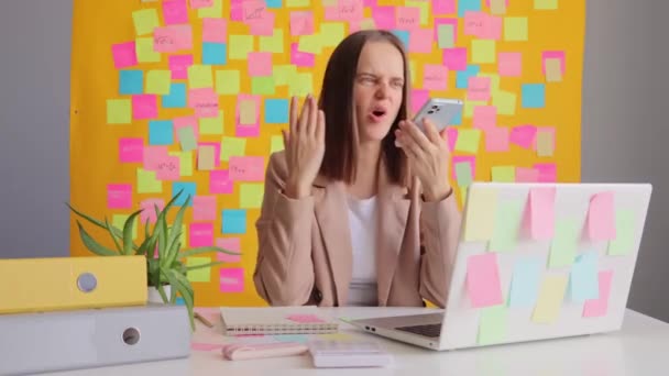 Rozzlobený Agresivní Mladá Žena Bundě Drží Telefon Zatímco Sedí Pracovišti — Stock video