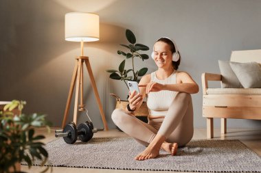 Kulaklıklı güzel bir kadın akıllı telefona bakıyor, müzik dinliyor ve antrenmandan sonra spor kıyafetlerini giyip spor yapıyor..