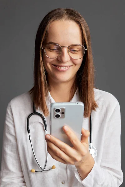 Virtual healthcare consultation. Telemedicine for medical care. Happy woman doctor wearing white medical lab coat stethoscope and glasses using smart phone for online consultation.
