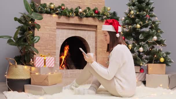 Красива Молода Жінка Теплому Светрі Капелюсі Санта Клауса Сидить Вітальні — стокове відео