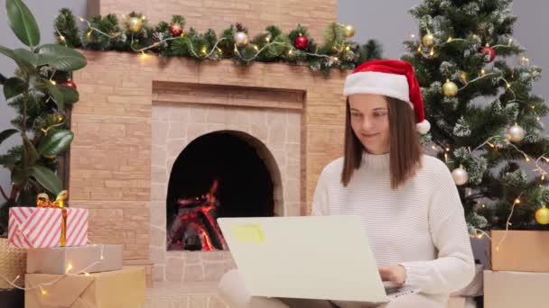 Ευτυχισμένη Γυναίκα Φορώντας Πουλόβερ Και Άγιος Βασίλης Καπέλο Χρησιμοποιώντας Φορητό — Αρχείο Βίντεο