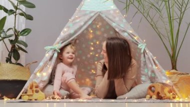Çocukluk ve ebeveynlik. Küçük çocuğuyla yerde yatan sevimli gülümseme. Annesi, küçük kızıyla evde oynuyordu. Mutluluğunu ifade ederken eğleniyordu..
