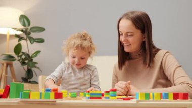 Oyun yoluyla bilişsel gelişim. Geometrik oyuncak keşfi. Yeni yürümeye başlayan çocuk şekil öğreniyor. Tahta istifleme oyunu. Beyaz kadın, küçük kızıyla iç mekanda oynuyor..