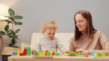 Şekil ayırıcı sorunu. Eğlenceli hareketler. Tahta yığını. Geometrik oyuncak keşfi. Sevimli genç anne, yeni yürümeye başlayan kızıyla evin içinde oynuyor..