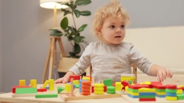Çocukluk motor becerileri. Ufaklığın renkli oyunu Ufaklığın gelişimi. Çocuk dostu bulmacalar. Bebek bebek, evin içindeki masada tahta geometrik oyuncaklarla oynuyor..
