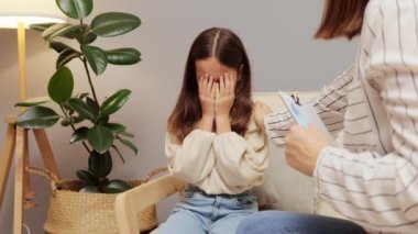 Çocuk psikoloğu ile terapi seansında ağlayan duygusal kız anaokulu öğrencisini teselli eden tanınmayan bir kadın küçük bir hastaya yardım etmeye çalışıyor..