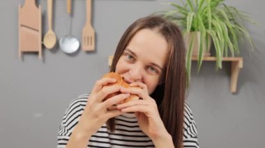 Akşam yemeğinde kahverengi saçlı, burgerci çekici bir kadın öğle yemeğinde abur cubur yemeyi, çizgili tişörtünü giyip lezzetli bir hamburger yemeyi tercih ediyor..