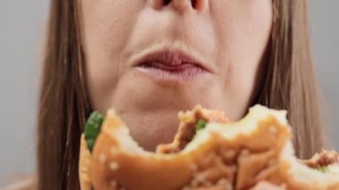 Düzgün beslenme, fast food, sağlıksız seçim. Büyük hamburgerleri yiyen, lezzetli fast food yemeklerinin tadını çıkaran, tanınmayan kahverengi saçlı kadının yakın çekimi..