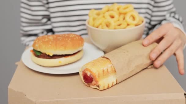ホットドッグ ハンバーガー オニオンスナック不健康なランチとダンボール箱を保持するストライプシャツの認識できない女性のクローズアップ — ストック動画