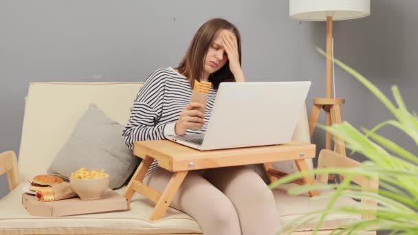 그녀의 거실에서 편안한 소파에 노트북과 테이크 패스트 푸드와 핫도그 지루한 — 비디오