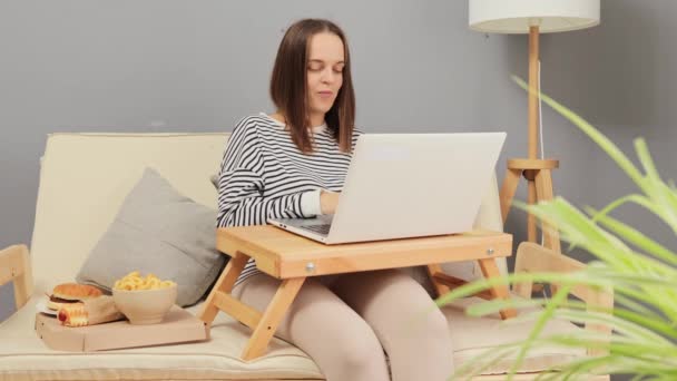 그녀의 거실에서 편안한 소파에 온라인 페이지를 노트북 테이크 패스트 푸드를 — 비디오