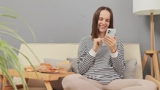 Mujer Relajada Positiva Feliz Sentada Sofá Comiendo Bocadillos Cebolla Usando — Vídeo de stock