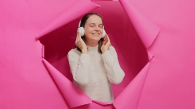 Neşeli, neşeli, gülümseyen, kulaklıkla müzik dinleyen, dans eden, favori müzik listesinin ya da radyonun keyfini çıkaran pembe kağıt deliğinde poz veren kadın..