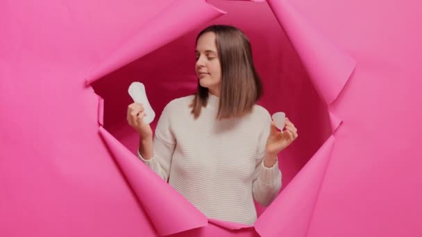Zdezorientowana Kobieta Trzyma Kubek Menstruacyjny Serwetkę Higieniczną Wybierając Artykuły Higieniczne — Wideo stockowe