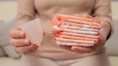 Kadın sağlığı için hijyen ürünü. Alternatif adet ürünleri. Tanınmayan bir kadın hijyen pedleri ve regl bardağı tutuyor, adet görüyor, seçim yapıyor.