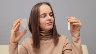 Samimi ve güvenli bir sağlık. Koleksiyoncu regl bardağı ve tampon gösteren neşeli bir kadın regl döneminde kullanmak için koruyucu ürünler seçiyor..