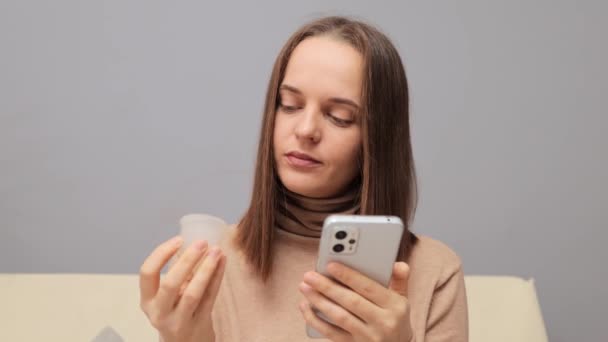 Συγκεντρωμένη Ενήλικη Νεαρή Γυναίκα Που Χρησιμοποιεί Κινητό Τηλέφωνο Και Κρατώντας — Αρχείο Βίντεο
