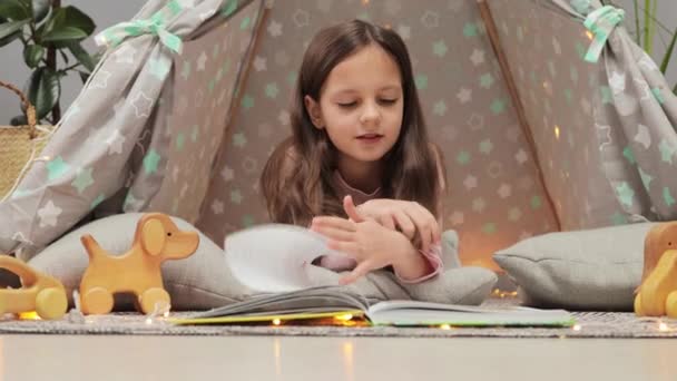 ダークヘアリーリーディングペーパーブックの奇妙な少女は 物語と新しい教科書を楽しんで 自宅のウィグワムの床に座っている写真を見ているページを回す — ストック動画