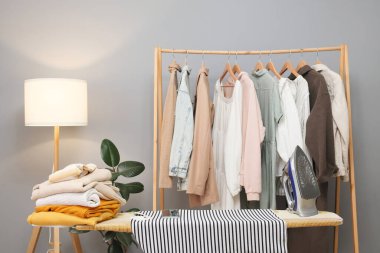 Askılarda yeni elbiseler ve ütü masasında evde giysi ütülemek için boş çalışma alanı.