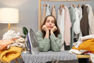 Ev ütüleme rutini. Ev gardırobu bakımı. Sıkıcı, üzgün, yetişkin bir kadın. Günlük gömlekler giyiyor. Çamaşır yıkadıktan sonra ev işlerini yapıyor.