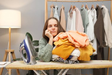 Sıkıcı, kahverengi saçlı, örgü gömlekli, ütülü elbiseli, başını kaldırıp kameraya bakan kadının ev işi yapacak havası yok.