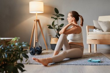 Aerobik ve esneme hareketleri. Egzersiz yapan güzel kadın. Spor giyim sektöründe çekici bir kadın. Spor yapan atletik kadın oturma odasında esneme egzersizleri yapıyor.