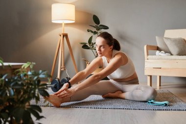 Atletik kız içeride egzersiz yapıyor. Evde spor ve yoga. Kapalı alandaki sağlık egzersizleri. Spor kıyafetli yetişkin bir kadın evde spor egzersizleri yapıyor. Oturma odasında egzersiz yapıyor.