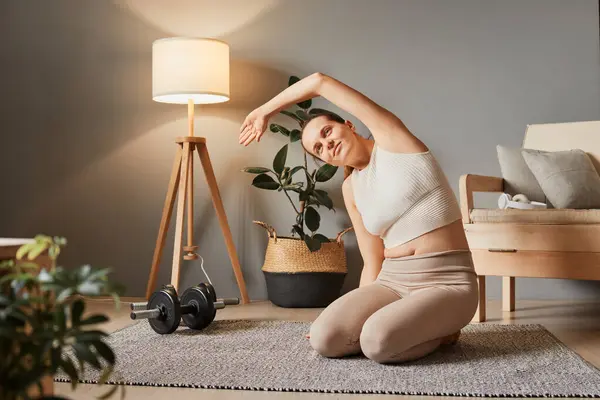 Athletic exercising indoors. Gym and yoga at home. Energy in indoor fitness. Body workout on the floor. Woman in sportswear doing fitness stretching exercises at home in the living room