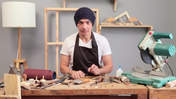 Jovem Carpinteiro Vestindo Avental Marrom Boné Sua Marcenaria Sentado Seu — Vídeo de Stock