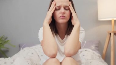 Mutsuz, kahverengi saçlı, üzgün bir kadın. Acı veren şakaklarına masaj yapıyor. Korkunç baş ağrısı belirtileri gösteriyor.