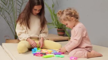 Kil ile okul öncesi eğitim. Yaratıcı modellik birlikte. Aile plastikçilik seansı. Evin iç kısımlarında plastik kalıplarla oynayan sevimli iki kız kardeş.