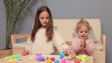 Okul öncesi yaratıcılık. Kardeş heykeli eğlencesi. Çocuk dostu zanaat zamanı. Plastik şişlikler ve şekiller. Komik iki küçük kız kardeş evde plastik kalıp figürleriyle oynuyorlar.