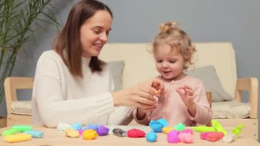 Anaokulunda oyun hamuru. Hamurlu, eğitici bir el işi. Anne yaratıcılığı öğretiyor. Neşeli sevimli beyaz kız ve anne evde renkli kil plastikle oynuyorlar.