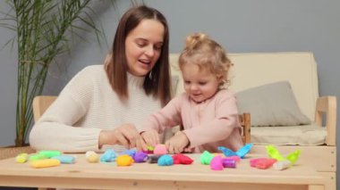 Oyun odası heykeli. Yaratıcı öğrenme materyali. Çocuklar için heykel eğlencesi. Mutlu beyaz bir kız ve anne ev içinde renkli kil plastikçiliği oynuyorlar.