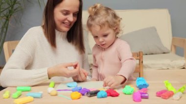 İnteraktif oyun hamuru oturumu. Duyusal öğrenme deneyimi. Yaratıcı bebek keşfi. Beyaz kız ve anne, evin içinde renkli kil plastikçiliği oynuyorlar.