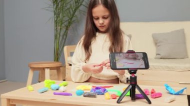 Esmer küçük kız plastiklerle oynuyor. Farklı figürler. Evde yaptığı yaratıcı çalışmaların videosunu çekiyor.