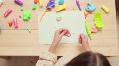 Çocuklar için masa aktiviteleri. Sanat ve eğitim birleşimi. Evde yaratıcı bir oyun. Eğitici oyuncakçılık. Renkli plastik parçalarla oynayan tanınmayan küçük bir kız gökkuşağı yapıyor.