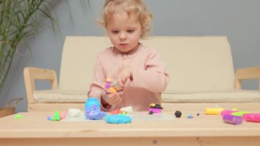 Renkli kreş aktiviteleri. Yetenek geliştirme oyunu. El yapımı bebek oyuncakları. Sevimli, beyaz, sarışın, dalgalı, küçük kız evde plastikle oynuyor.