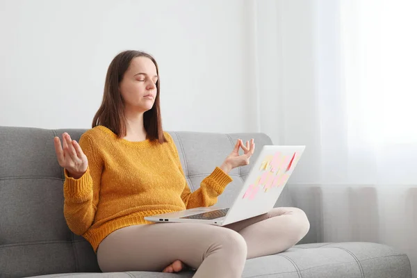 Using a laptop for remote work. Yoga for relaxing during work. Freelancer in a virtual workspace. Caucasian woman using laptop sitting on sofa at home