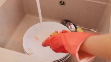 Tanımlanamayan bir temizlikçi elinde sünger, bulaşıkları içeride yıkıyor evdeki temizlik işine aktif olarak katılan sıvı deterjanla lavaboda camları yıkıyor.