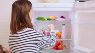 Hoşnutsuz kadın ev hanımı çizgili tişört giyiyor. Kötü yemek ile esrar içiyor. Ev mutfağında açık buzdolabının yanında duran berbat kokulu yemekler.